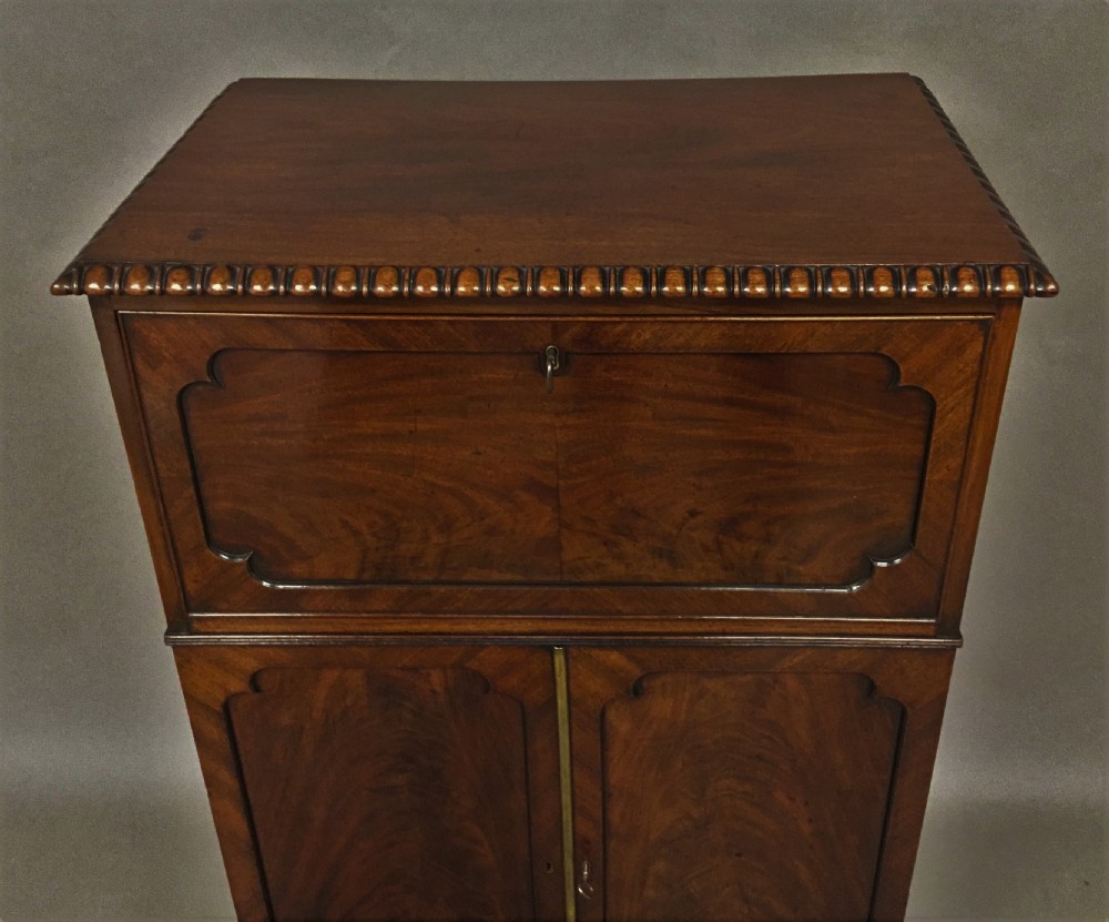 A Regency period mahogany secretaire cabinet featuring flame mahogany veneered doors with re-entrant corners, gadrooned borders, and bracket feet. View XXII