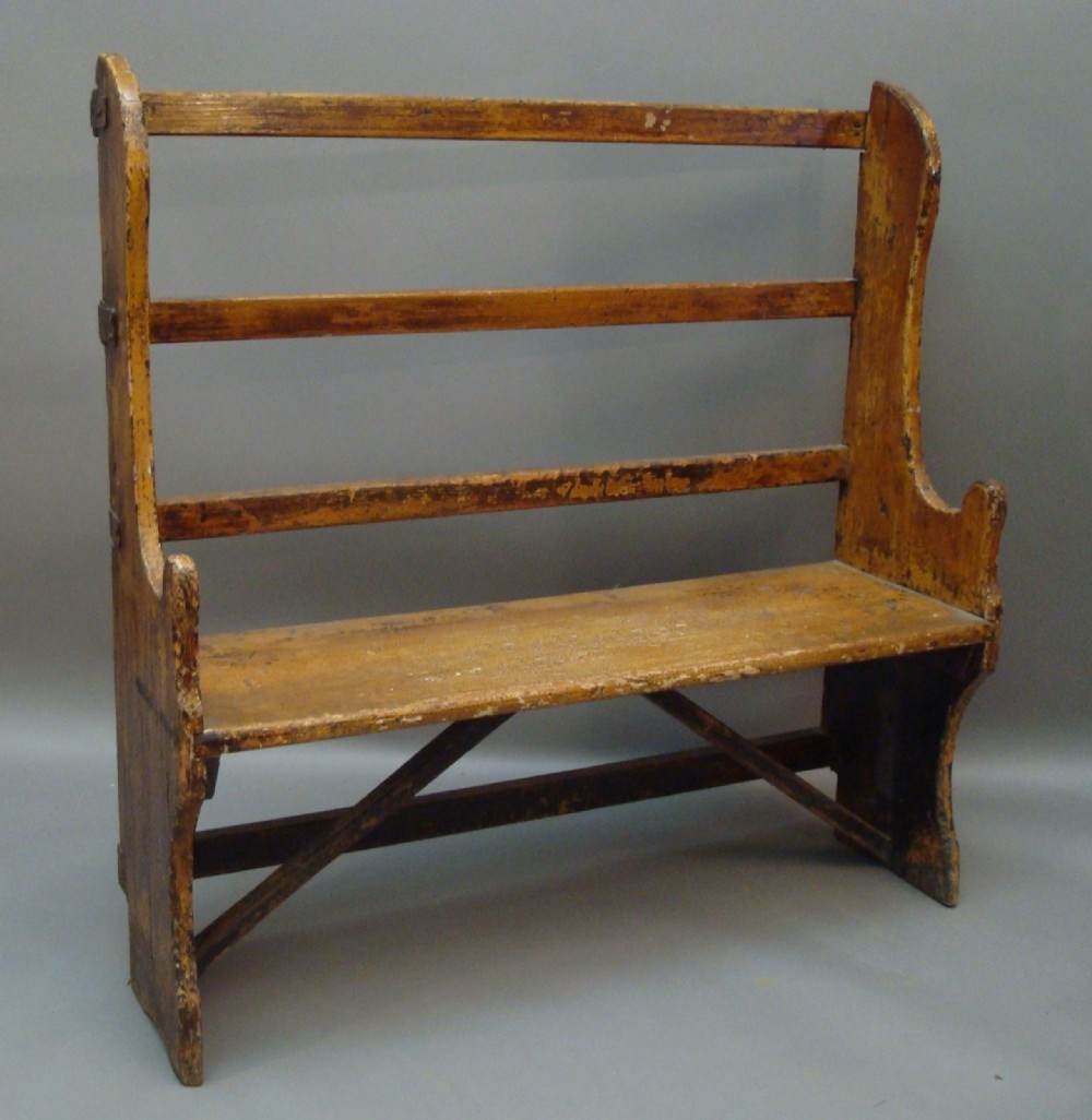 A Georgian primitive pine settle with a high open slat back, shaped side wings, and a warm scumble finish.