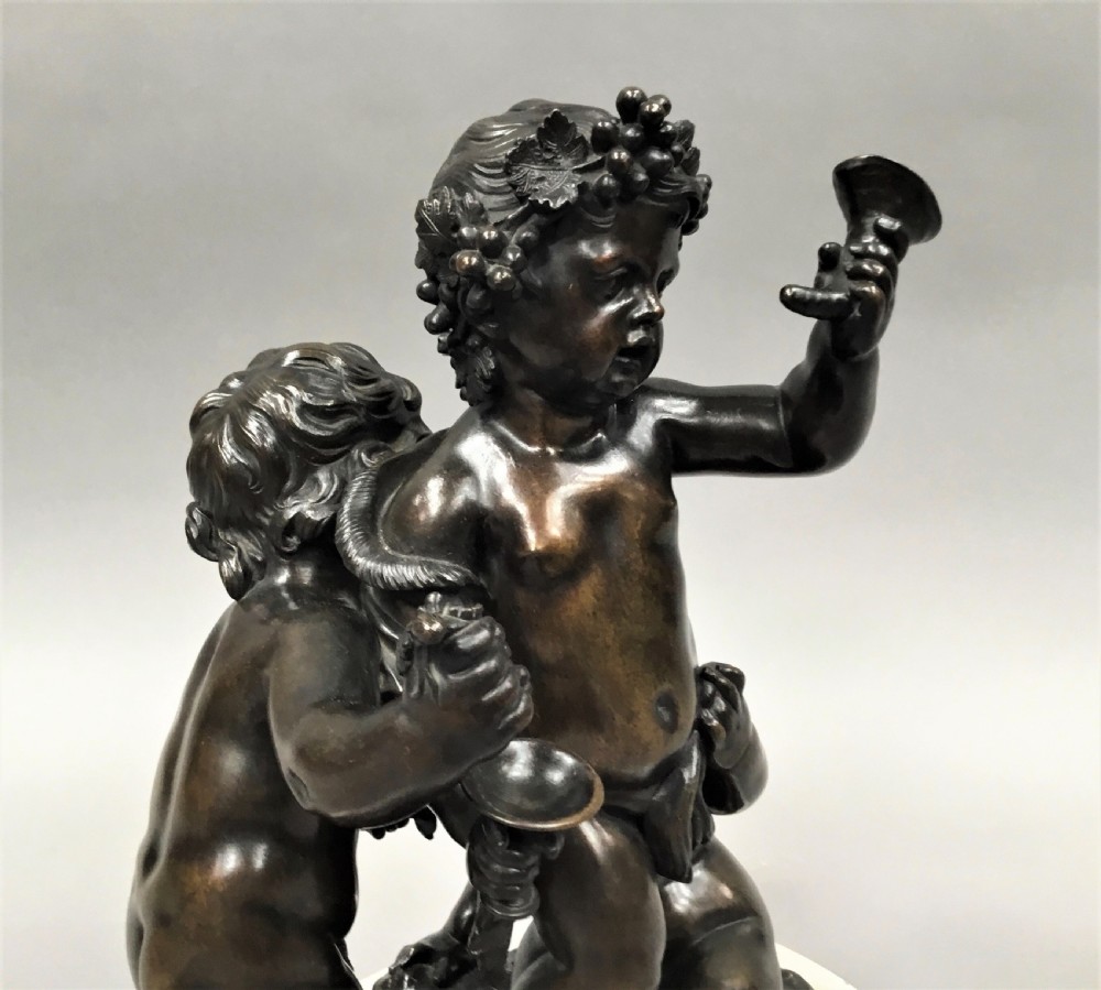 A nineteenth-century dark bronze sculpture depicting three Bacchanalian putti with grape clusters and cups, mounted on a circular white marble plinth. View XIII