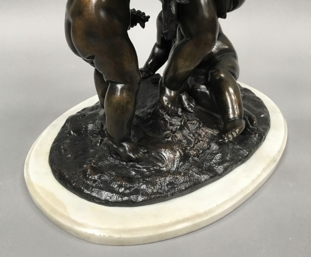 A nineteenth-century dark bronze sculpture depicting three Bacchanalian putti with grape clusters and cups, mounted on a circular white marble plinth. View XVI