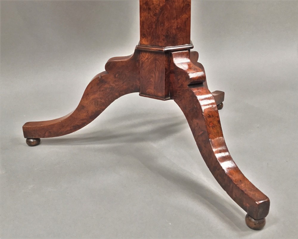 A Regency period tilt-top centre table made from burr yew wood, featuring a circular top displayed vertically on a tripod pedestal base with brass castors. View IV