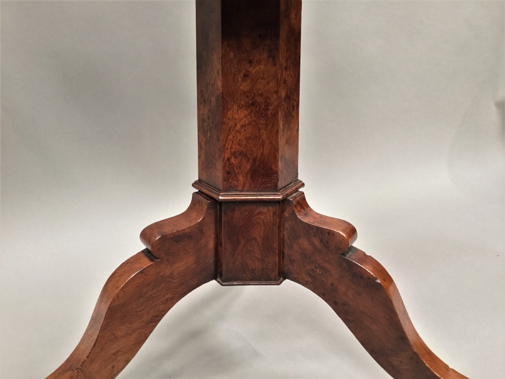A Regency period tilt-top centre table made from burr yew wood, featuring a circular top displayed vertically on a tripod pedestal base with brass castors. View VIII