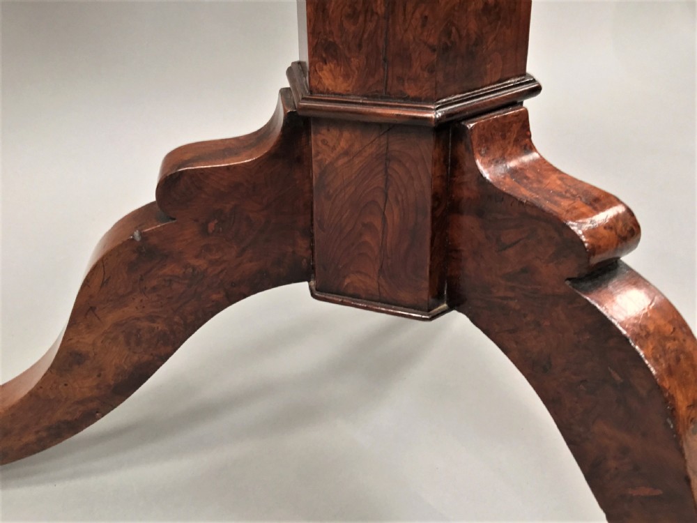 A Regency period tilt-top centre table made from burr yew wood, featuring a circular top displayed vertically on a tripod pedestal base with brass castors. View X