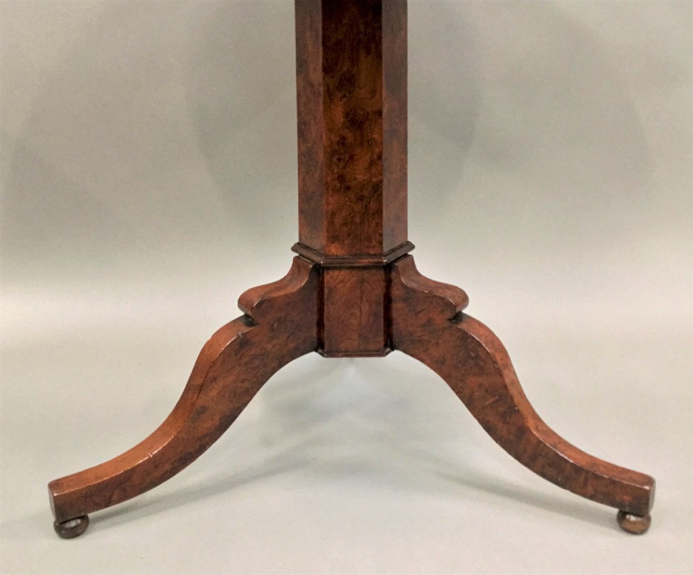 A Regency period tilt-top centre table made from burr yew wood, featuring a circular top displayed vertically on a tripod pedestal base with brass castors. View XI