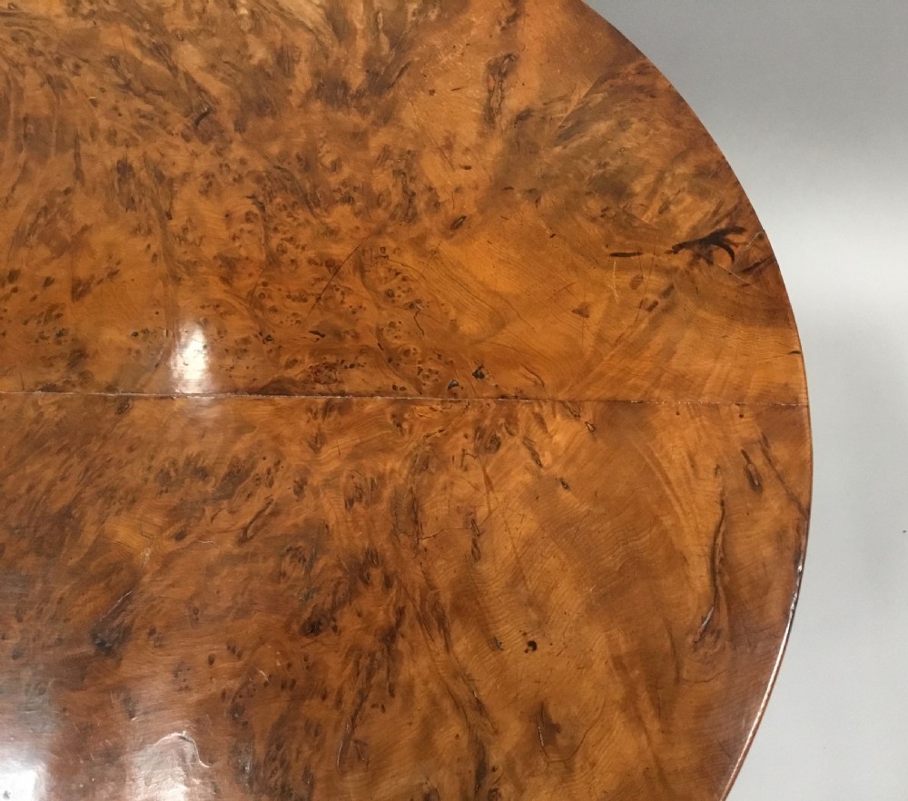 A Regency period tilt-top centre table made from burr yew wood, featuring a circular top displayed vertically on a tripod pedestal base with brass castors. View XIV