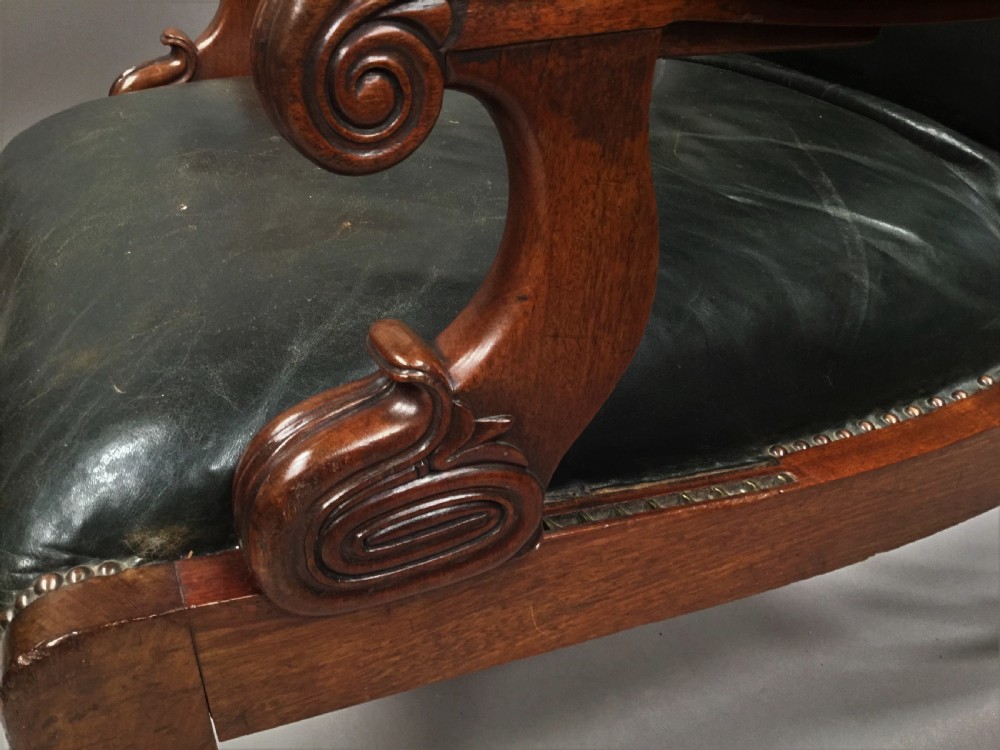 A Late Regency mahogany library armchair with dark green button-backed leather upholstery, carved scroll arms, and reeded front legs on brass castors. View XIII