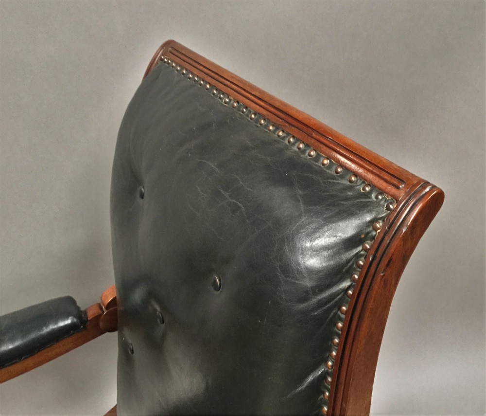 A Late Regency mahogany library armchair with dark green button-backed leather upholstery, carved scroll arms, and reeded front legs on brass castors. View XVII