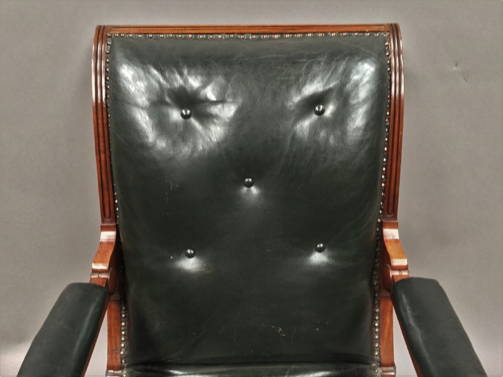 A Late Regency mahogany library armchair with dark green button-backed leather upholstery, carved scroll arms, and reeded front legs on brass castors. View XXI