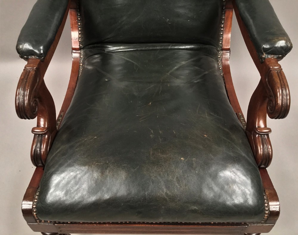 A Late Regency mahogany library armchair with dark green button-backed leather upholstery, carved scroll arms, and reeded front legs on brass castors. View XXII
