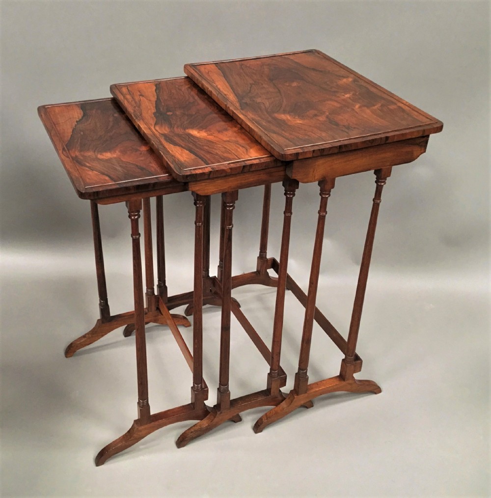 A set of three graduated Regency rosewood nesting tables featuring turned twin-spindle legs and trestle feet.