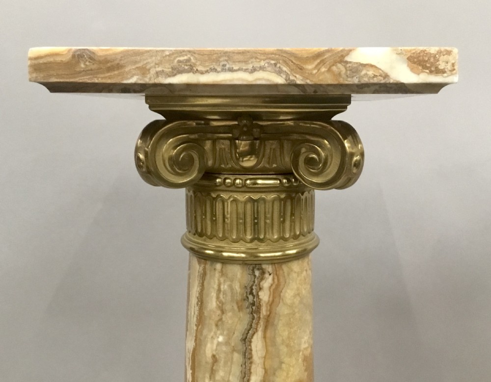 A pair of nineteenth-century Neoclassical pedestals featuring veined beige marble shafts, brass ormolu Ionic capitals, and square marble bases. View V