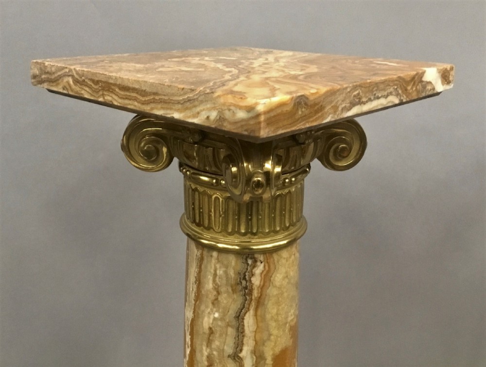 A pair of nineteenth-century Neoclassical pedestals featuring veined beige marble shafts, brass ormolu Ionic capitals, and square marble bases. View XXIV