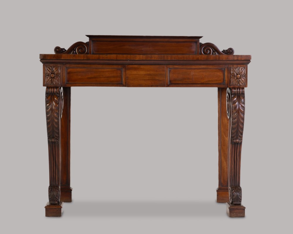 A Late Regency mahogany console table featuring a raised gallery back, carved acanthus leaf scroll legs, and rosette corner blocks.