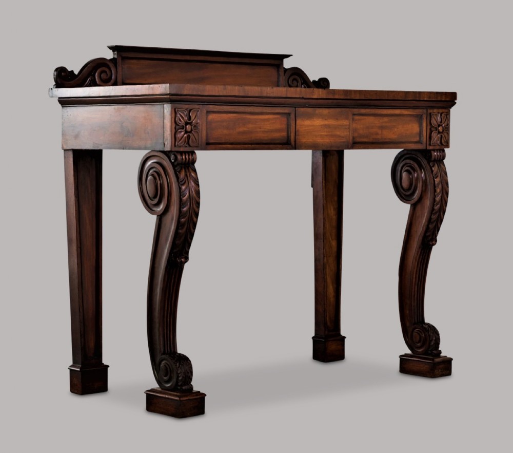 A Late Regency mahogany console table featuring a raised gallery back, carved acanthus leaf scroll legs, and rosette corner blocks. View II