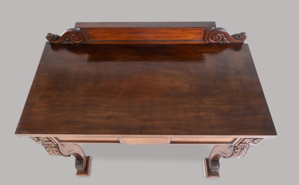 A Late Regency mahogany console table featuring a raised gallery back, carved acanthus leaf scroll legs, and rosette corner blocks. View III