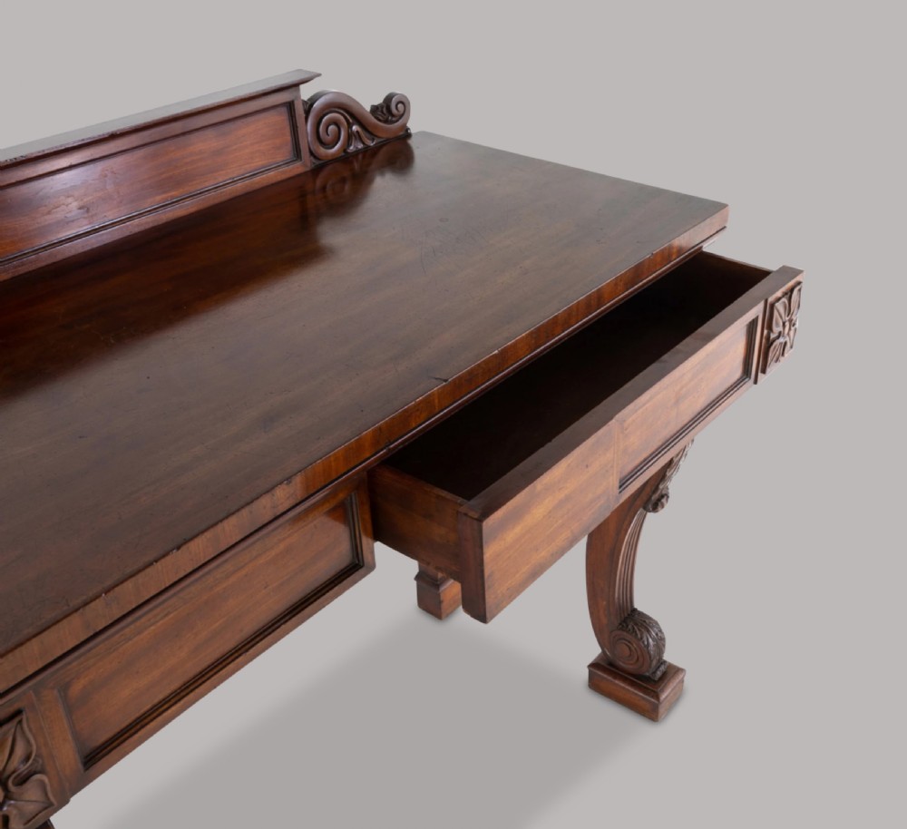 A Late Regency mahogany console table featuring a raised gallery back, carved acanthus leaf scroll legs, and rosette corner blocks. View IV