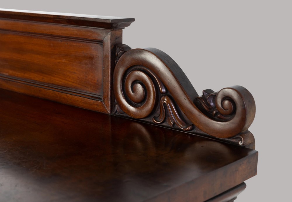 A Late Regency mahogany console table featuring a raised gallery back, carved acanthus leaf scroll legs, and rosette corner blocks. View V