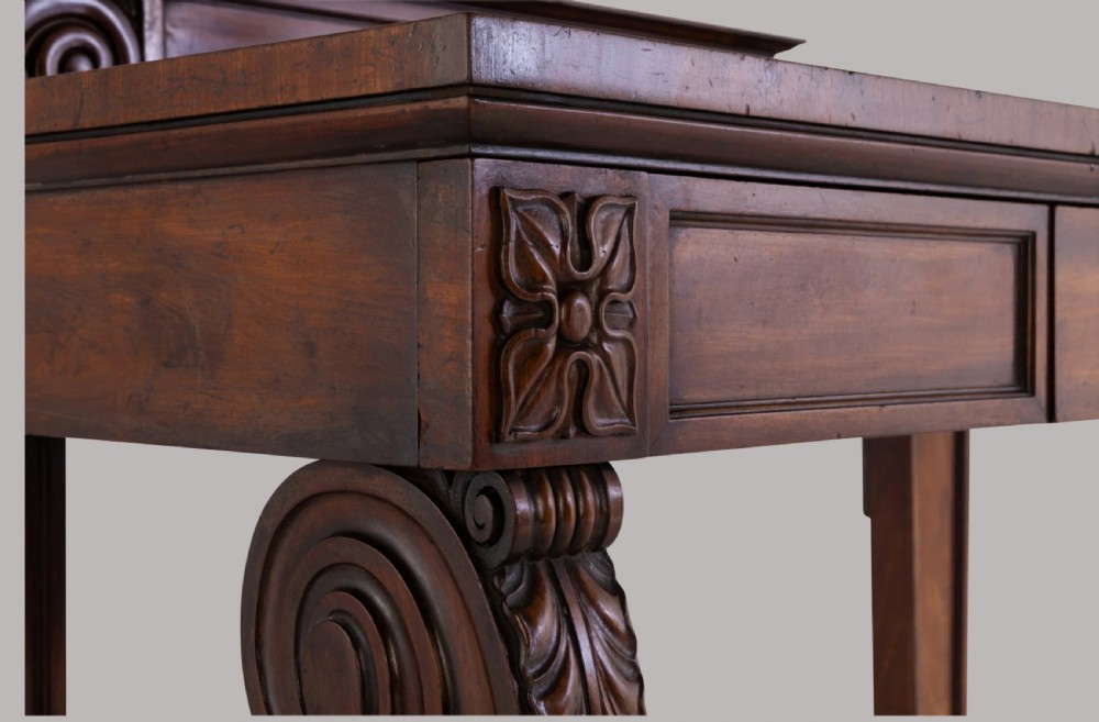 A Late Regency mahogany console table featuring a raised gallery back, carved acanthus leaf scroll legs, and rosette corner blocks. View VII
