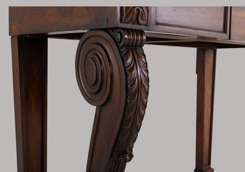 A Late Regency mahogany console table featuring a raised gallery back, carved acanthus leaf scroll legs, and rosette corner blocks. View VIII