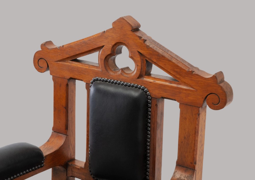A pair of 19th-century Gothic Revival golden oak open armchairs with black leather upholstery and carved trefoil pediments. View V