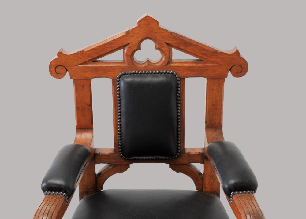 A pair of 19th-century Gothic Revival golden oak open armchairs with black leather upholstery and carved trefoil pediments. View VI