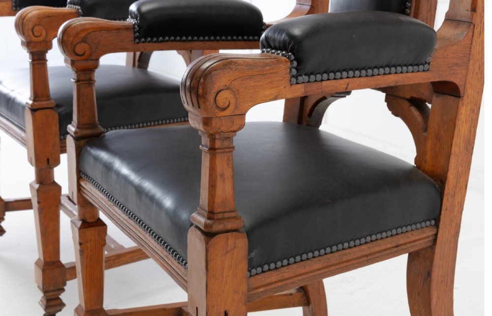 A pair of 19th-century Gothic Revival golden oak open armchairs with black leather upholstery and carved trefoil pediments. View X