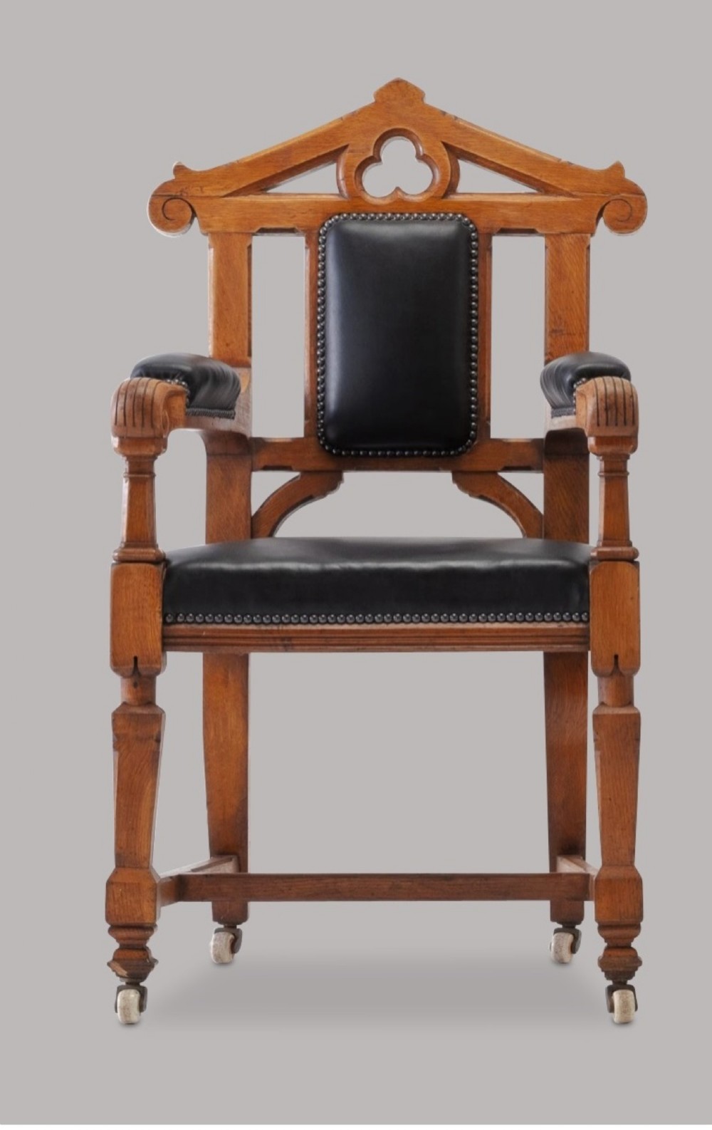 A pair of 19th-century Gothic Revival golden oak open armchairs with black leather upholstery and carved trefoil pediments. View XII