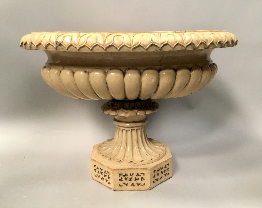 A cream glazed terracotta pedestal urn with a gadrooned lower bowl and an octagonal base featuring incised markings. View III