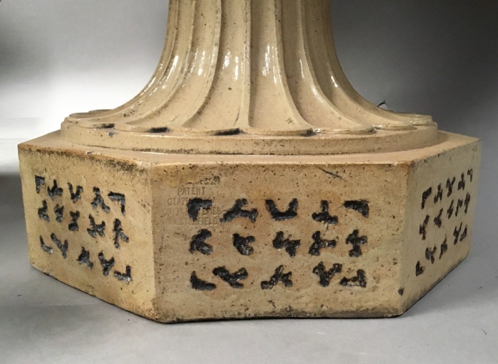 A cream glazed terracotta pedestal urn with a gadrooned lower bowl and an octagonal base featuring incised markings. View X
