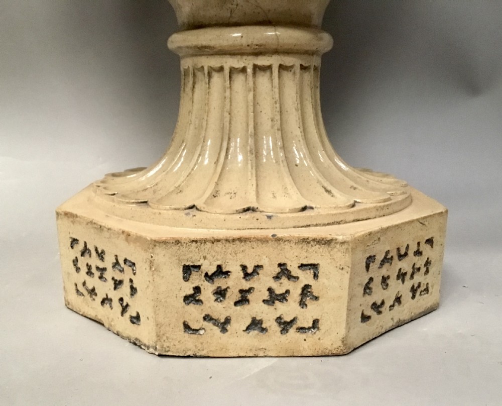A cream glazed terracotta pedestal urn with a gadrooned lower bowl and an octagonal base featuring incised markings. View XI