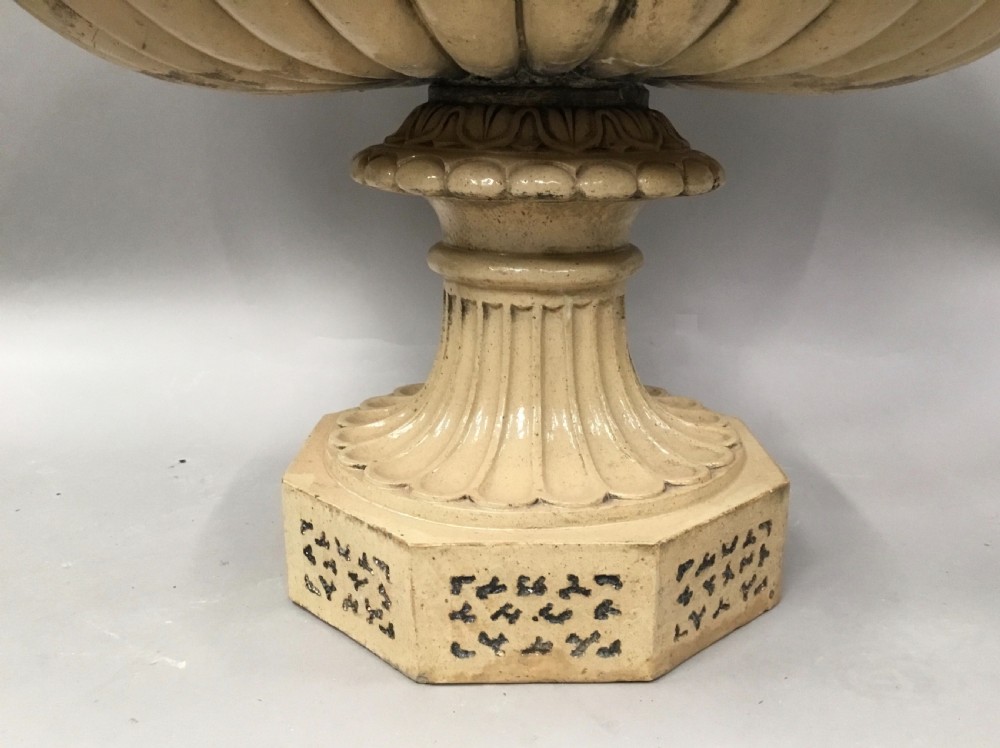A cream glazed terracotta pedestal urn with a gadrooned lower bowl and an octagonal base featuring incised markings. View XII