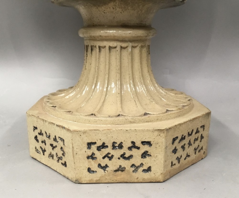 A cream glazed terracotta pedestal urn with a gadrooned lower bowl and an octagonal base featuring incised markings. View XIV