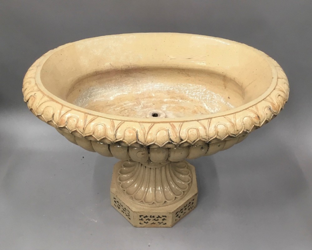 A cream glazed terracotta pedestal urn with a gadrooned lower bowl and an octagonal base featuring incised markings. View XVII