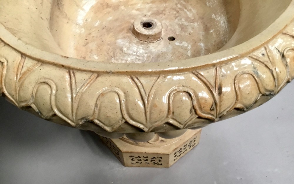 A cream glazed terracotta pedestal urn with a gadrooned lower bowl and an octagonal base featuring incised markings. View XX
