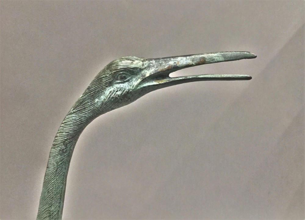 An early 20th-century cast bronze sculpture of a crane with an open beak and weathered verdigris green patina, standing on a textured base. View XVI