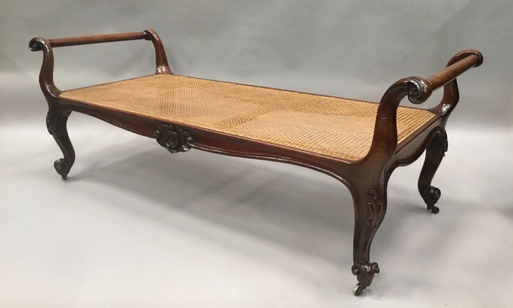 A mid-19th century mahogany window seat featuring a hand-woven cane panel, scrolled side handles, and carved cabriole legs with brass castors.