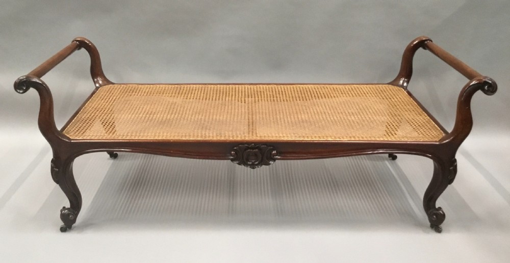 A mid-19th century mahogany window seat featuring a hand-woven cane panel, scrolled side handles, and carved cabriole legs with brass castors. View II