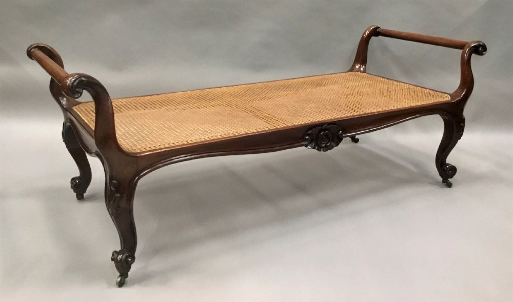 A mid-19th century mahogany window seat featuring a hand-woven cane panel, scrolled side handles, and carved cabriole legs with brass castors. View IV