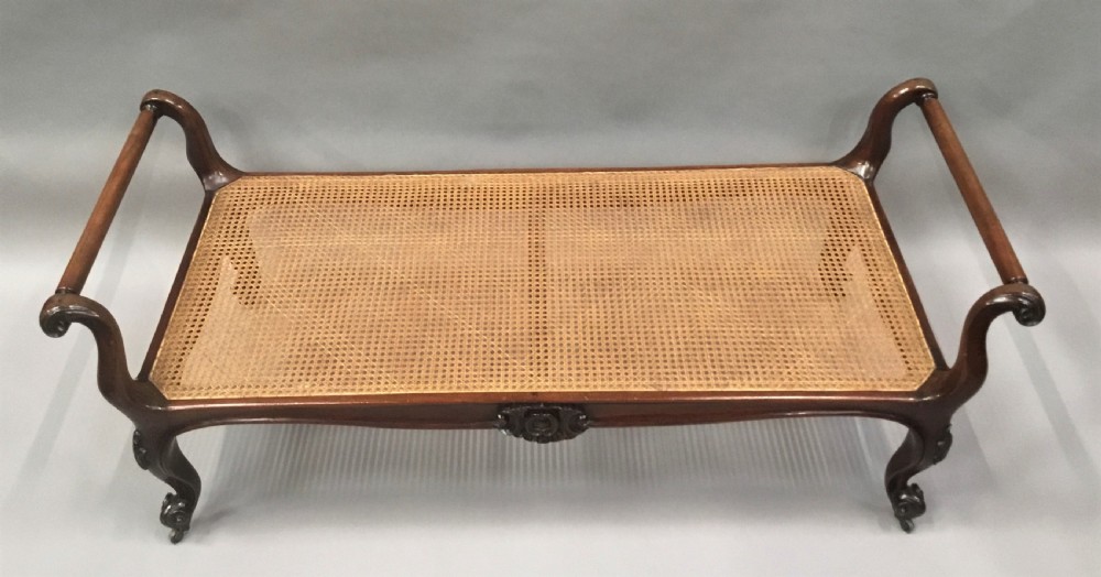 A mid-19th century mahogany window seat featuring a hand-woven cane panel, scrolled side handles, and carved cabriole legs with brass castors. View V