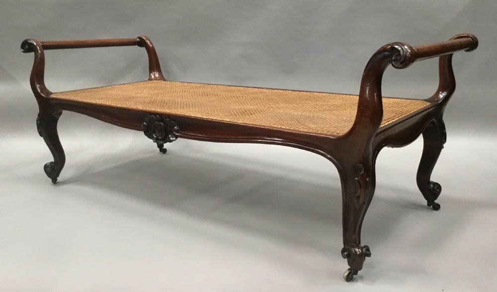 A mid-19th century mahogany window seat featuring a hand-woven cane panel, scrolled side handles, and carved cabriole legs with brass castors. View VI