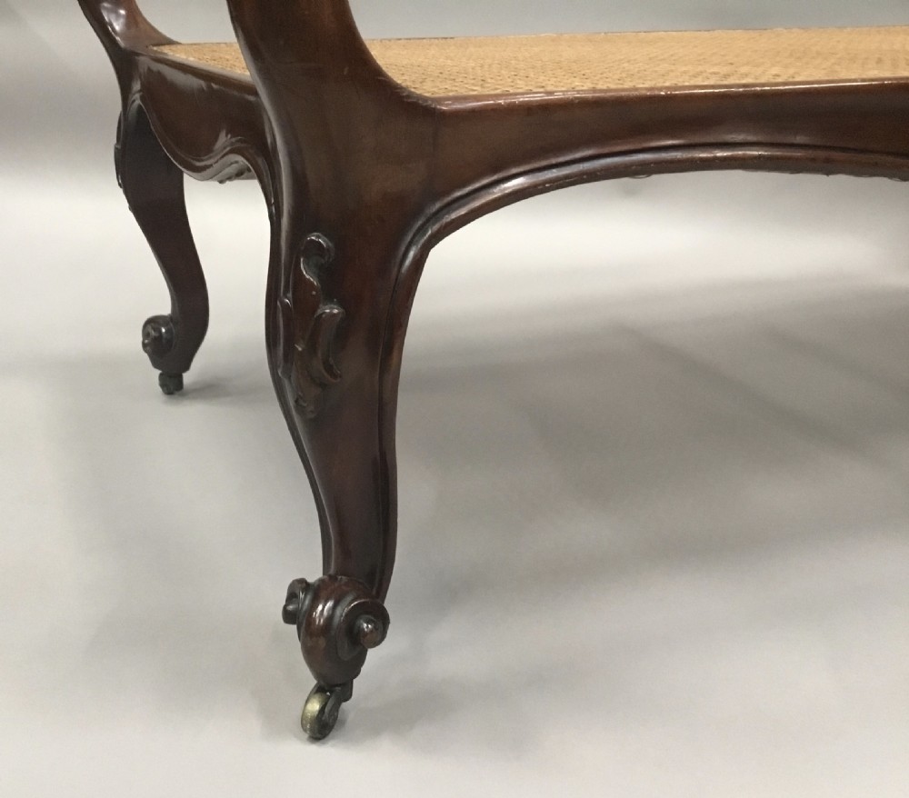 A mid-19th century mahogany window seat featuring a hand-woven cane panel, scrolled side handles, and carved cabriole legs with brass castors. View XIII