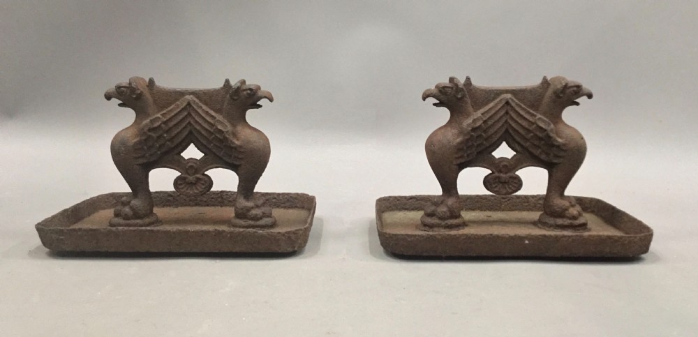 A pair of antique cast iron boot scrapers featuring sculpted griffin side supports and rectangular drip trays with an oxidised surface. View II