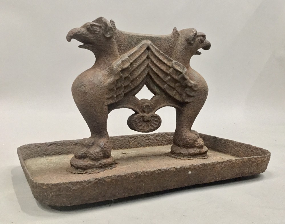 A pair of antique cast iron boot scrapers featuring sculpted griffin side supports and rectangular drip trays with an oxidised surface. View V