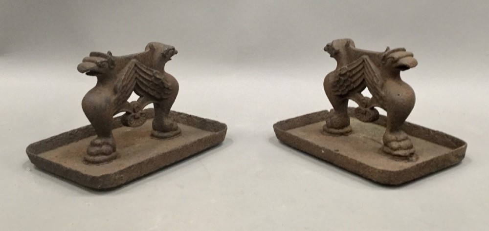 A pair of antique cast iron boot scrapers featuring sculpted griffin side supports and rectangular drip trays with an oxidised surface. View VI
