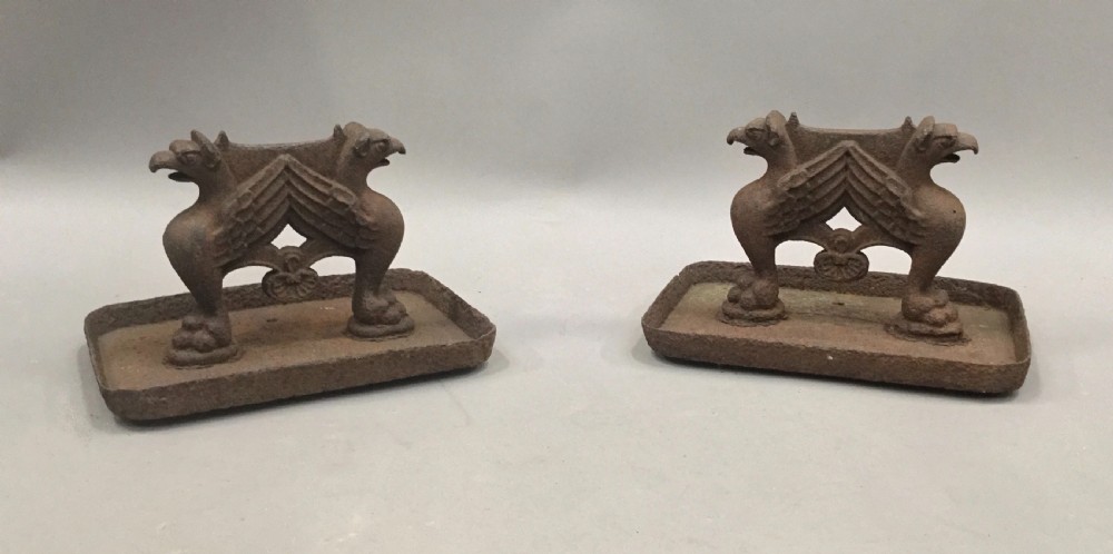 A pair of antique cast iron boot scrapers featuring sculpted griffin side supports and rectangular drip trays with an oxidised surface. View VII