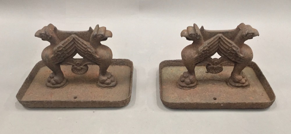 A pair of antique cast iron boot scrapers featuring sculpted griffin side supports and rectangular drip trays with an oxidised surface. View IX