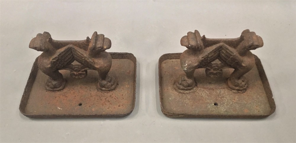 A pair of antique cast iron boot scrapers featuring sculpted griffin side supports and rectangular drip trays with an oxidised surface. View XI