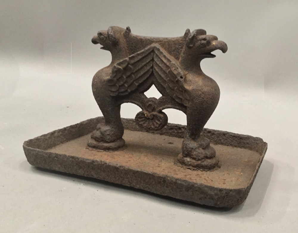 A pair of antique cast iron boot scrapers featuring sculpted griffin side supports and rectangular drip trays with an oxidised surface. View XIII