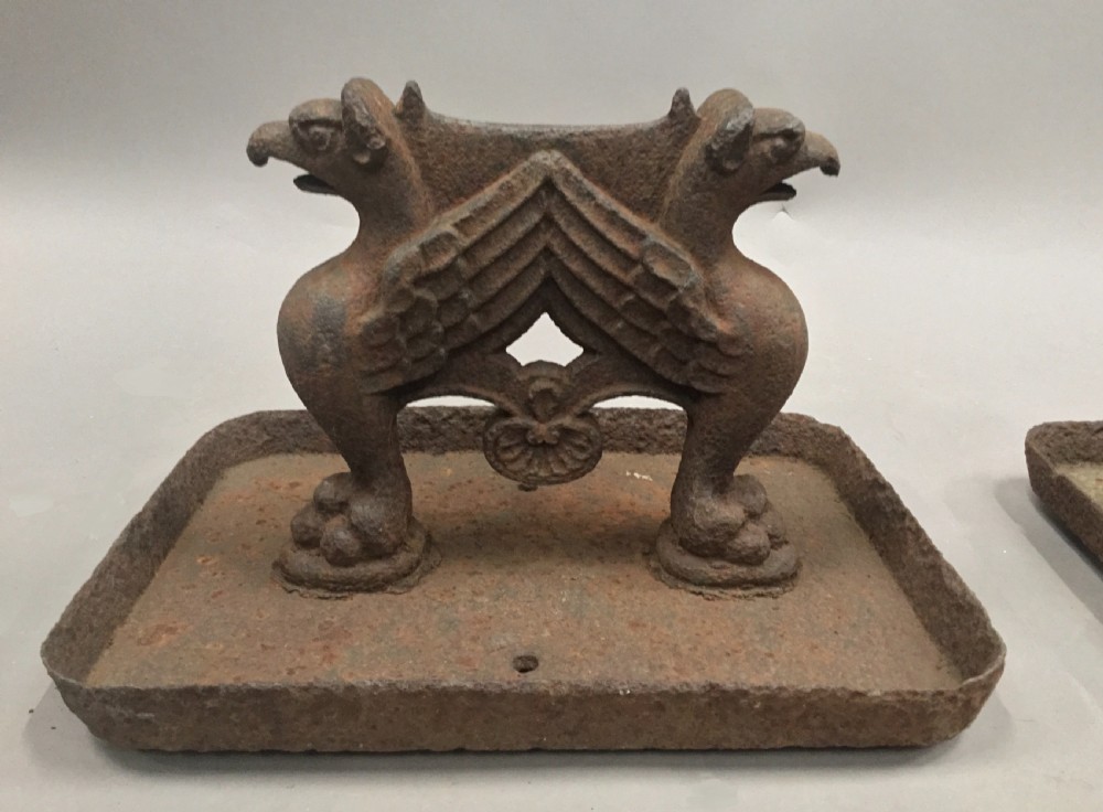 A pair of antique cast iron boot scrapers featuring sculpted griffin side supports and rectangular drip trays with an oxidised surface. View XIV