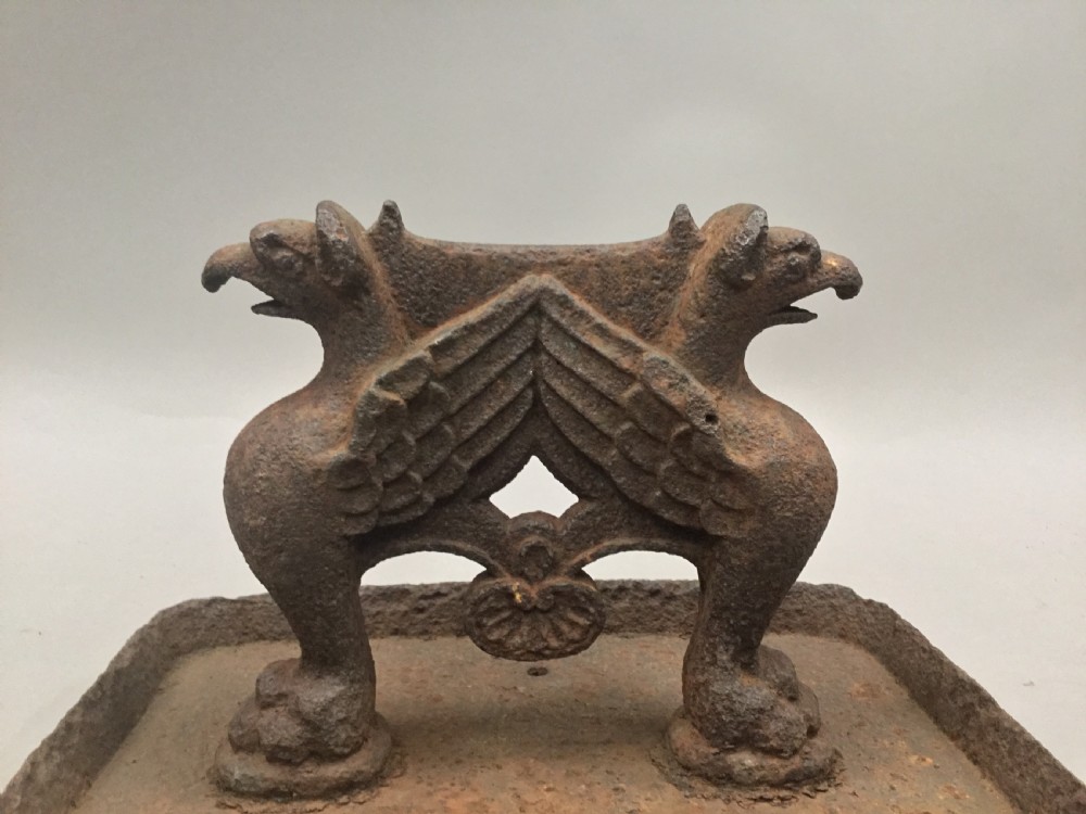 A pair of antique cast iron boot scrapers featuring sculpted griffin side supports and rectangular drip trays with an oxidised surface. View XV